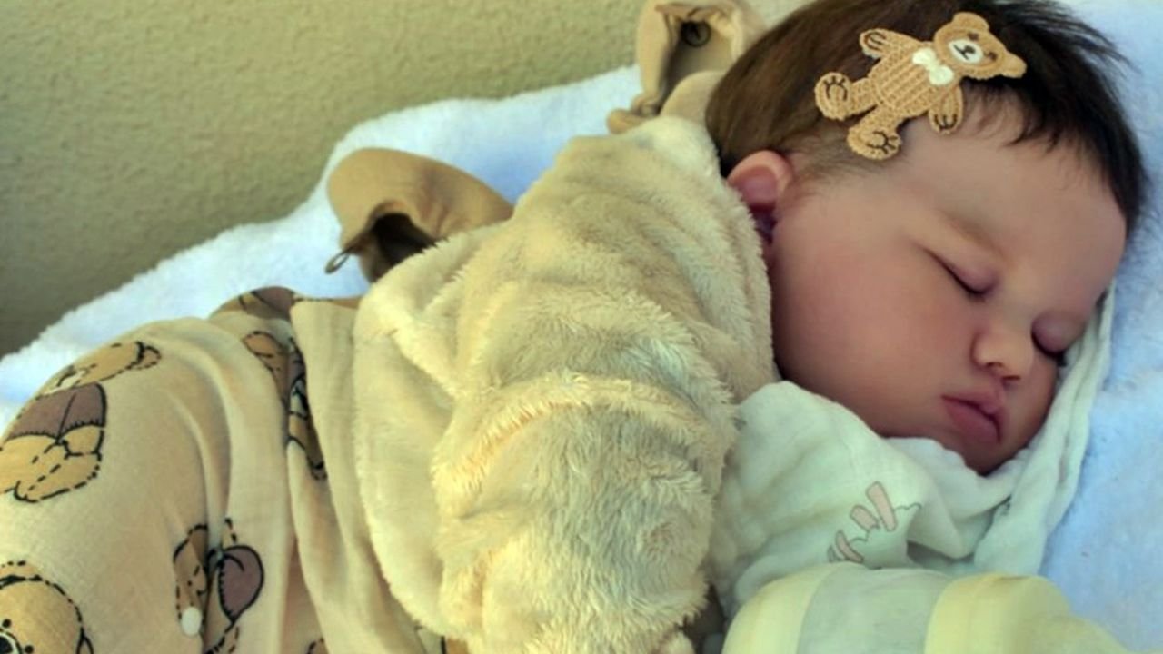 Bebê reborn recém-nascido dormindo profundamente em um cobertor macio, vestindo um macacão estampado com ursinhos.